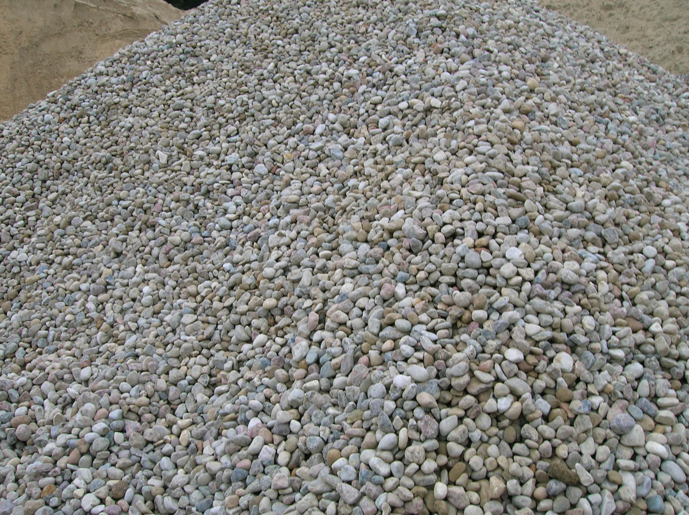 Góra drobnych, okrągłych kamieni o szaro-beżowej barwie, tworzących dużą pryzmę na placu budowy.